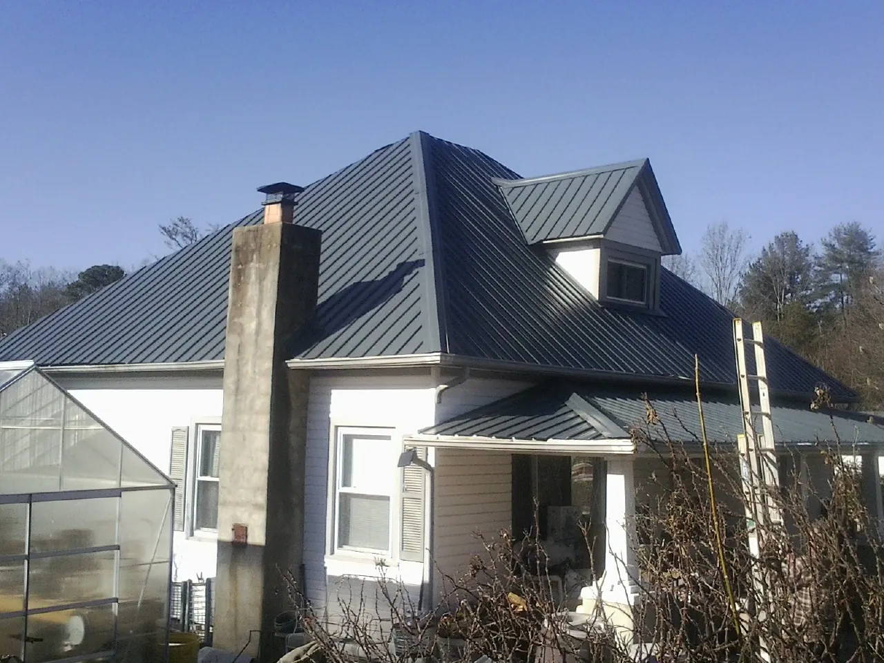 Dark blue standing seam metal roof on a white farmhouse with dormer — Slate & Tile Roof Repair by Roofing Brothers in Sabina