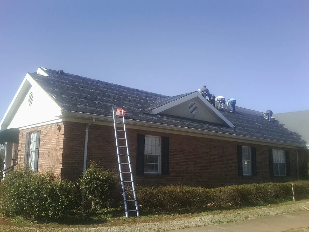 Crew tearing shingles off a brick ranch roof with a ladder set — Metal Roof Repair work by our crew in Sabina
