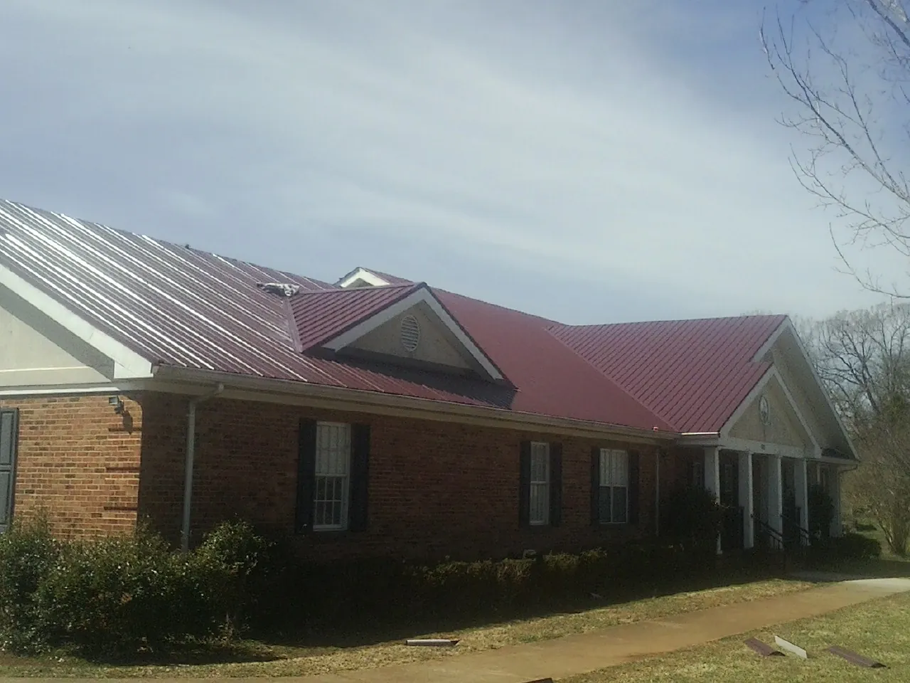Red metal roof with gabled entries on a long brick building, from a Hail Damage Roof Repair job in Sabina