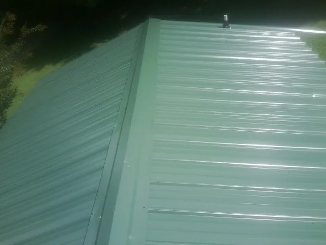 New green metal panels meeting at the ridge of a roof — Flat Roof Repair work by our crew in Sabina