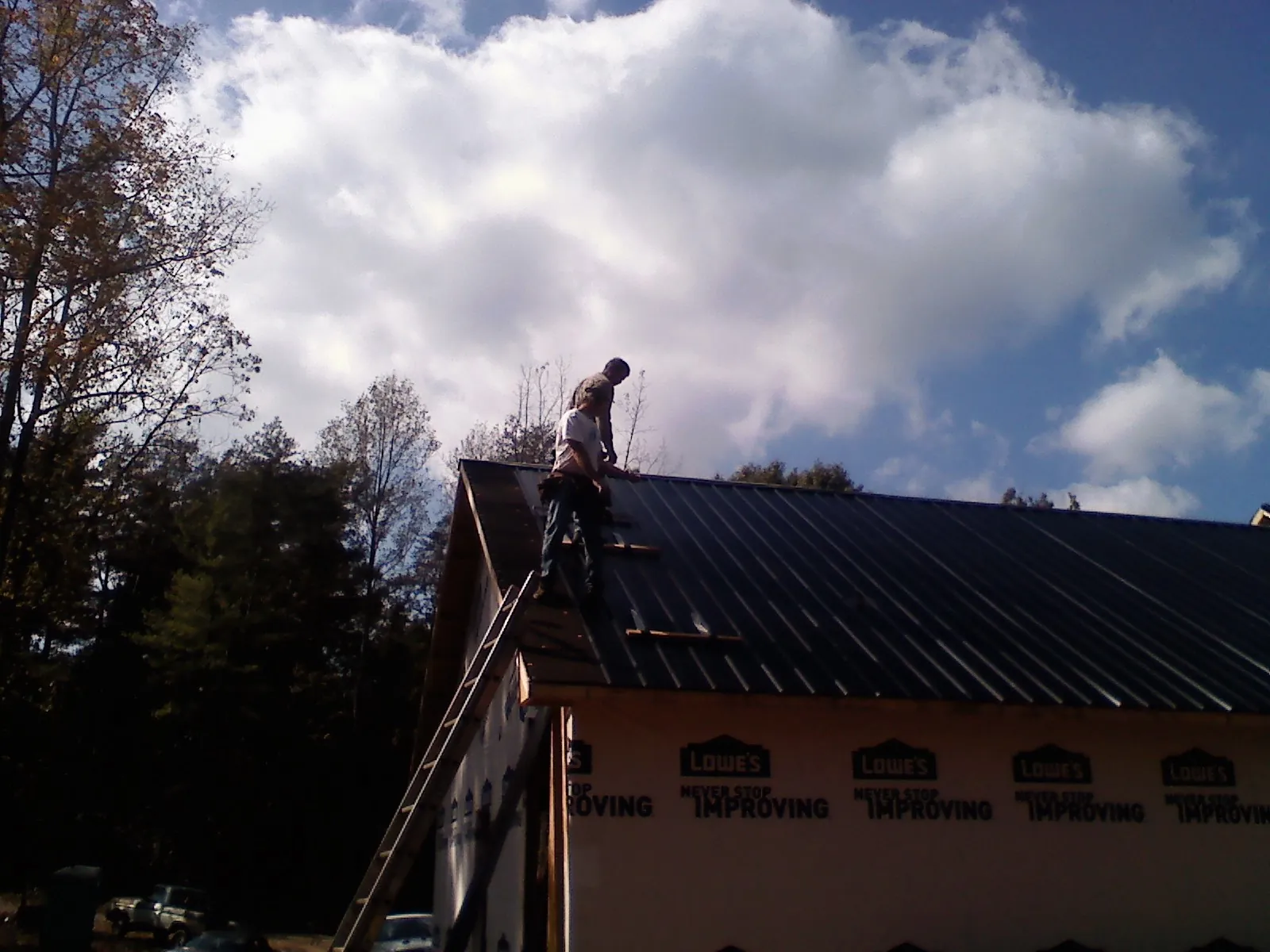 Roofer fastening dark metal panels high against a cloudy sky, from a Roof Inspection job in Sabina