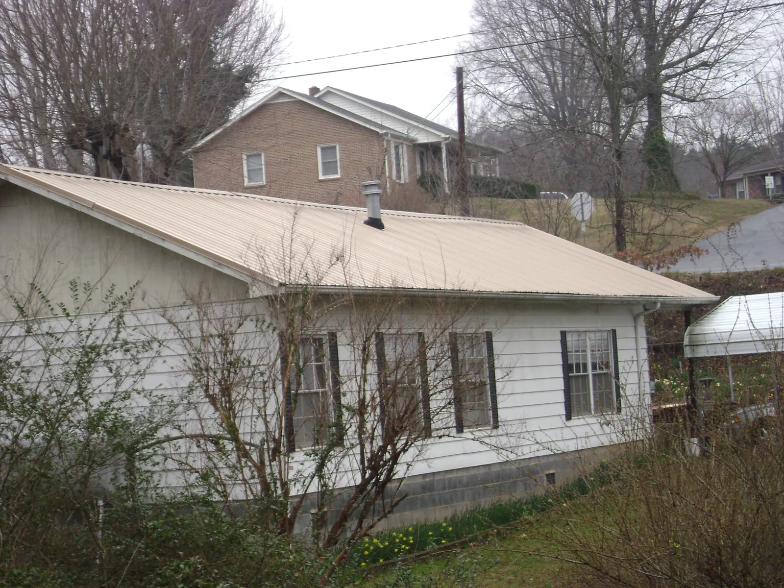 Tan metal roof on a white sided house set into a hillside — Commercial Roofing by Roofing Brothers in Sabina