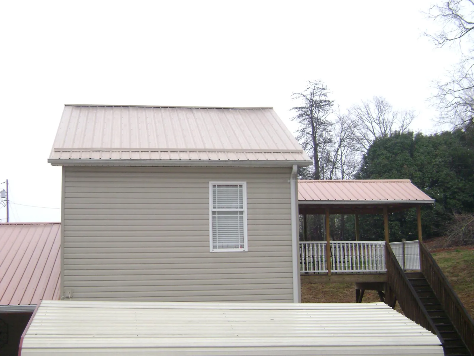 Tan metal roofs on a two story addition and attached porch, from a Roof Replacement job in Sabina